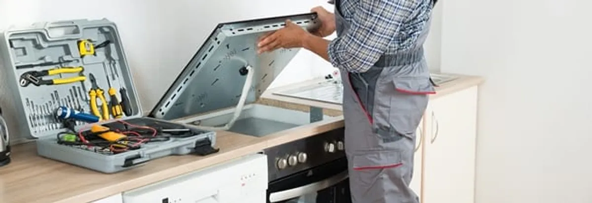 Cooktop repair technician lifting a built-in stovetop for service in Cedar Rapids, IA