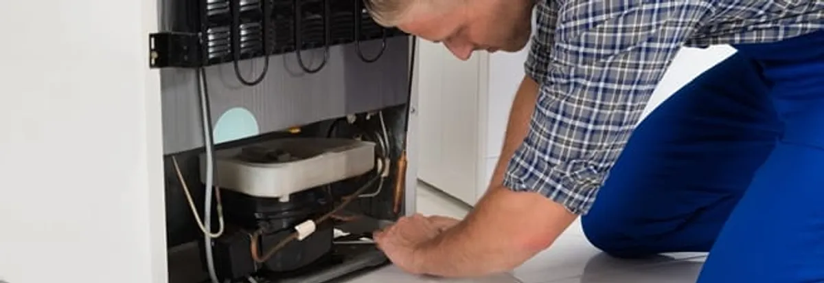 Refrigerator repair technician servicing the compressor and condenser area in Cedar Rapids, IA