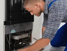 Refrigerator repair technician servicing the compressor and condenser area in Cedar Rapids, IA